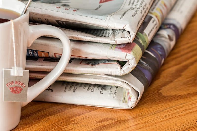 Stack of newspapers on a table with a cup of Five Roses tea.