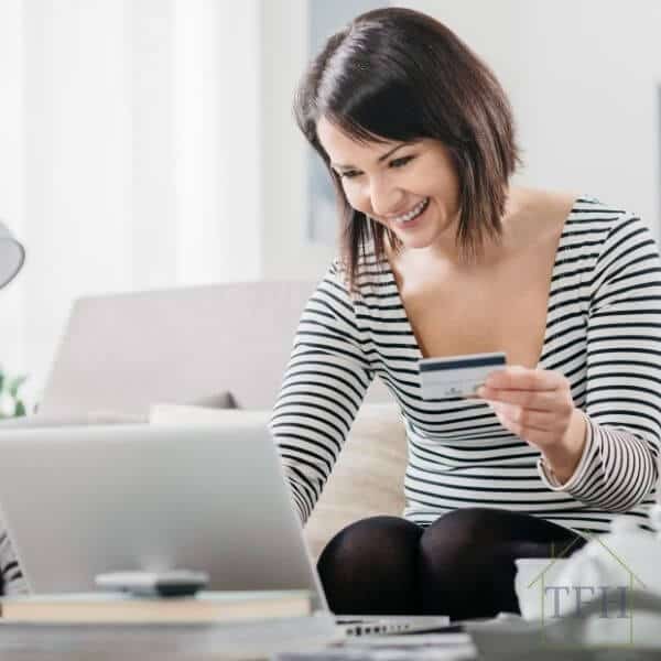 Woman dressed in black and white shirt with black pants, shopping on laptop holding credit card in her hand.