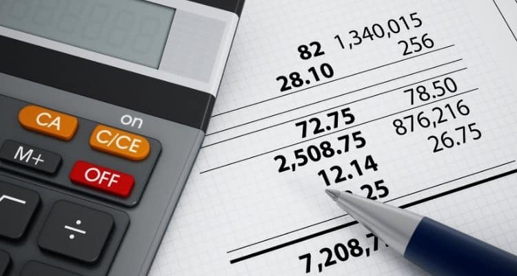 Calculator laying on a table beside a piece of paper showing account balances.